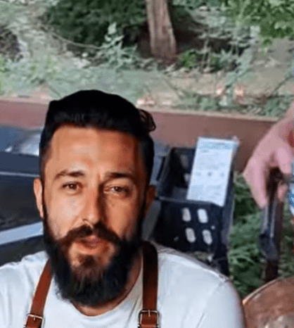 Man with a beard and mustache outdoors, smiling.