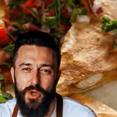 Man with a beard and mustache speaking, with a sandwich in the background.