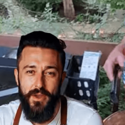 Man with a beard and mustache outdoors, smiling.